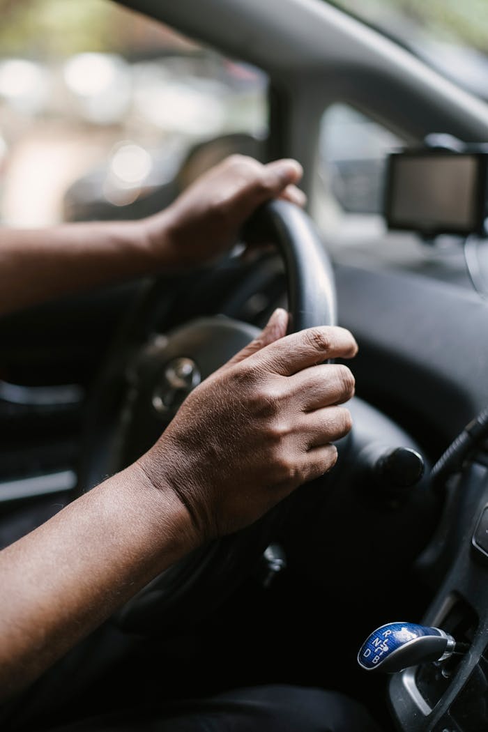 Crop unrecognizable person sitting in car with automatic transmission while holding steering wheel and driving